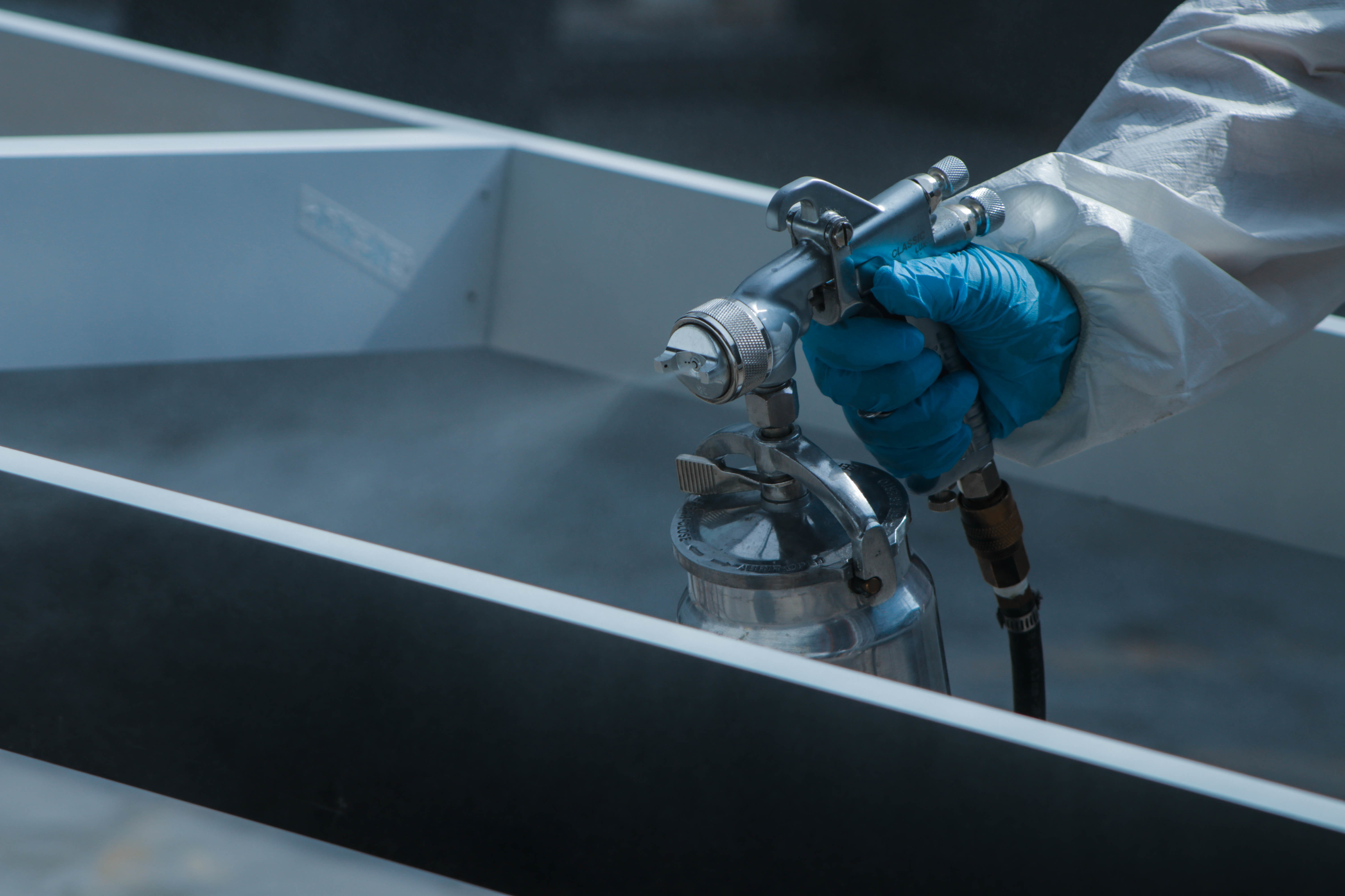 Technicien ACL Thermolaquage appliquant le revêtement en poudre sur une pièce métallique